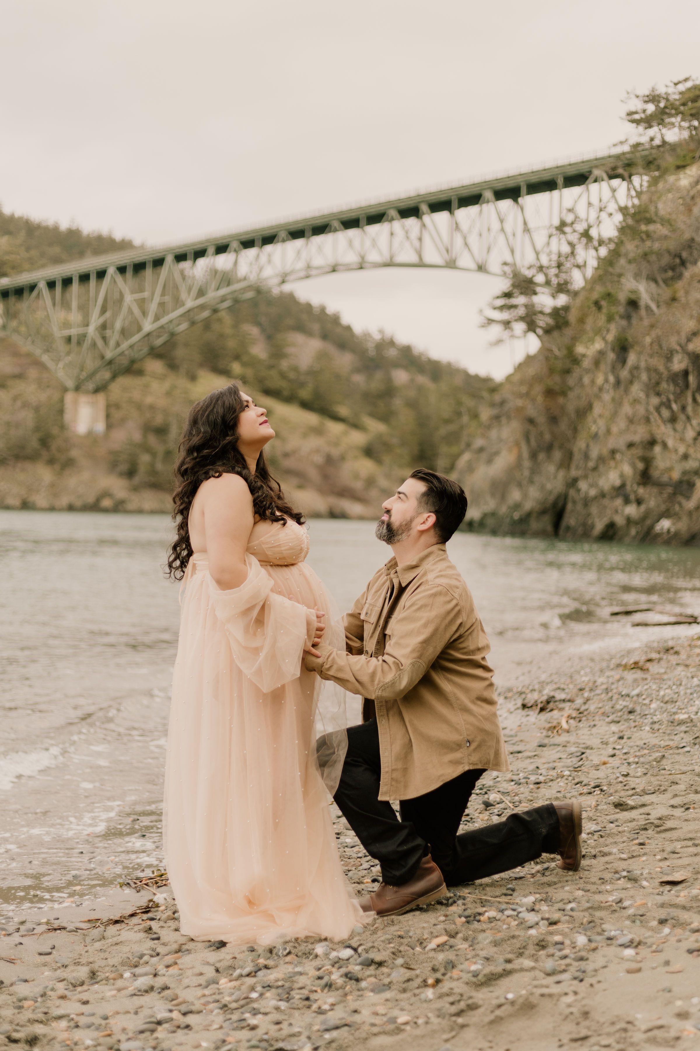 A romantic proposal scene with a scenic bridge view takes place on a rocky riverbank at Deception Pass.