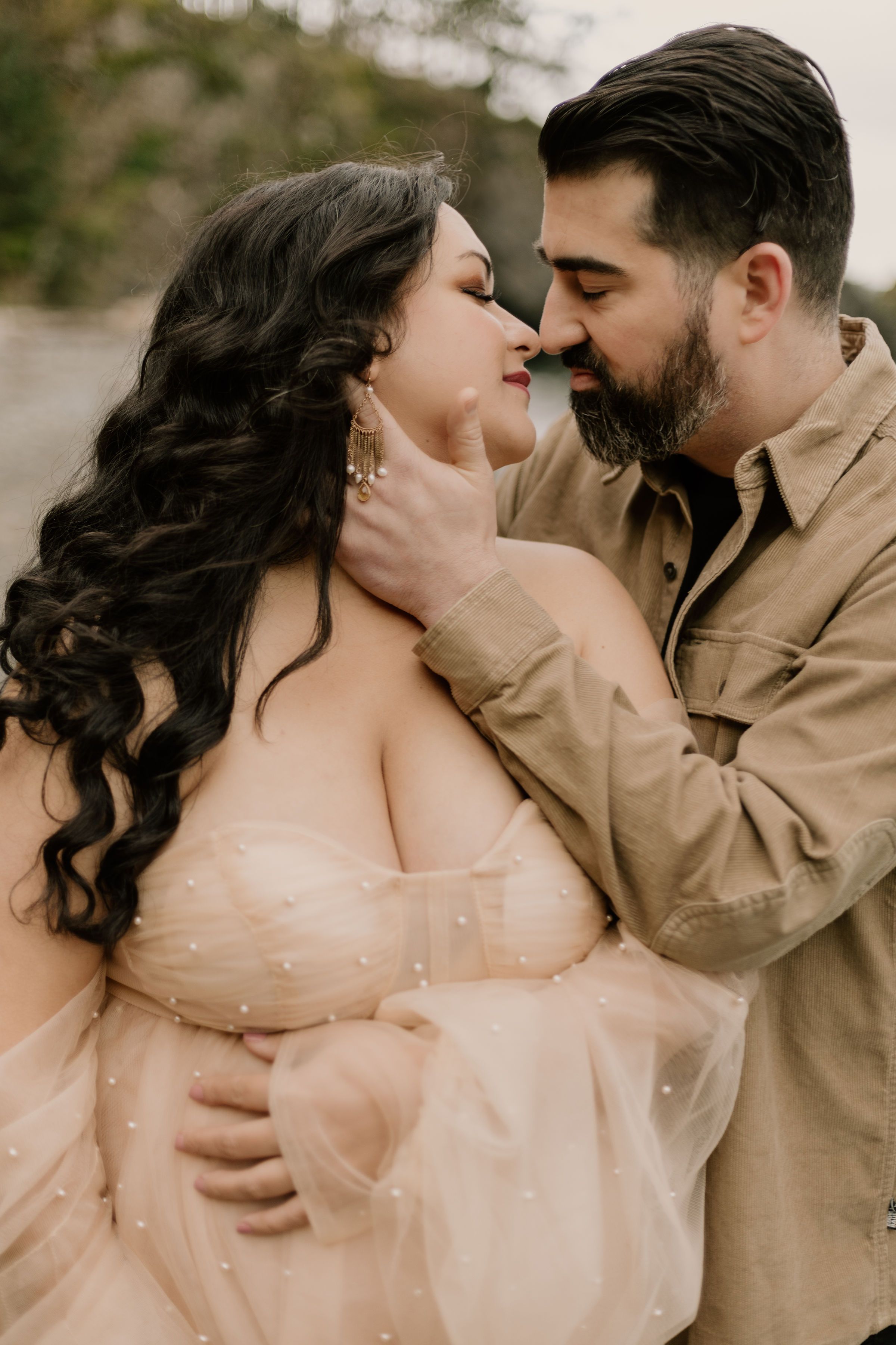 A romantic couple share an intimate moment in a dreamy outdoor setting, with her wearing a flowy blush gown.