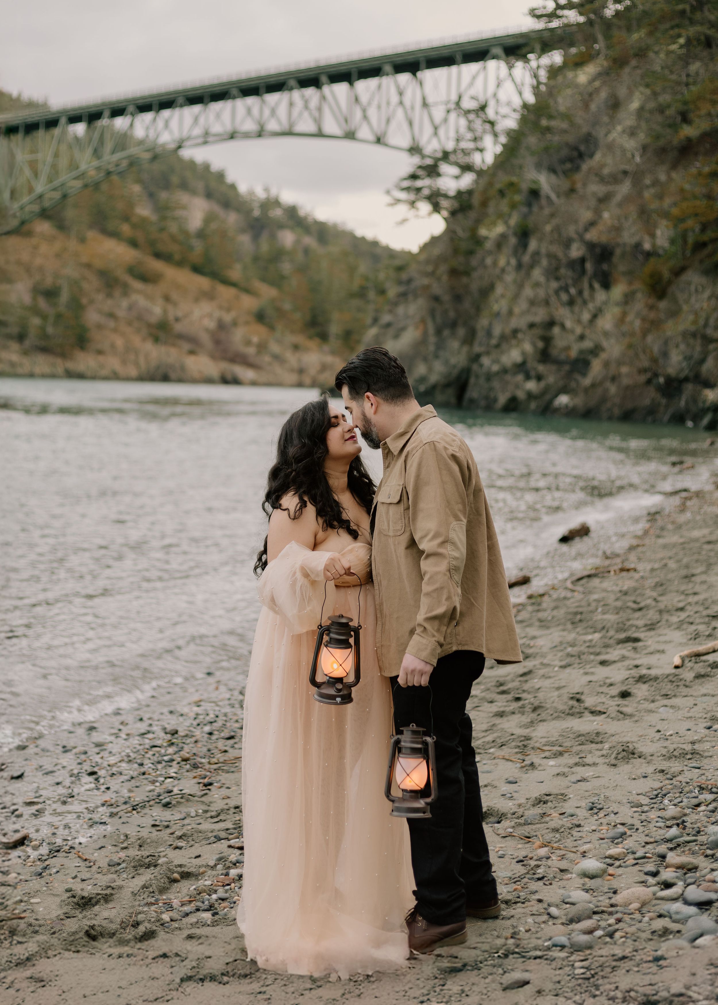 A romantic couple shares an intimate moment on a rocky beach at sunset, illuminated by glowing lanterns.