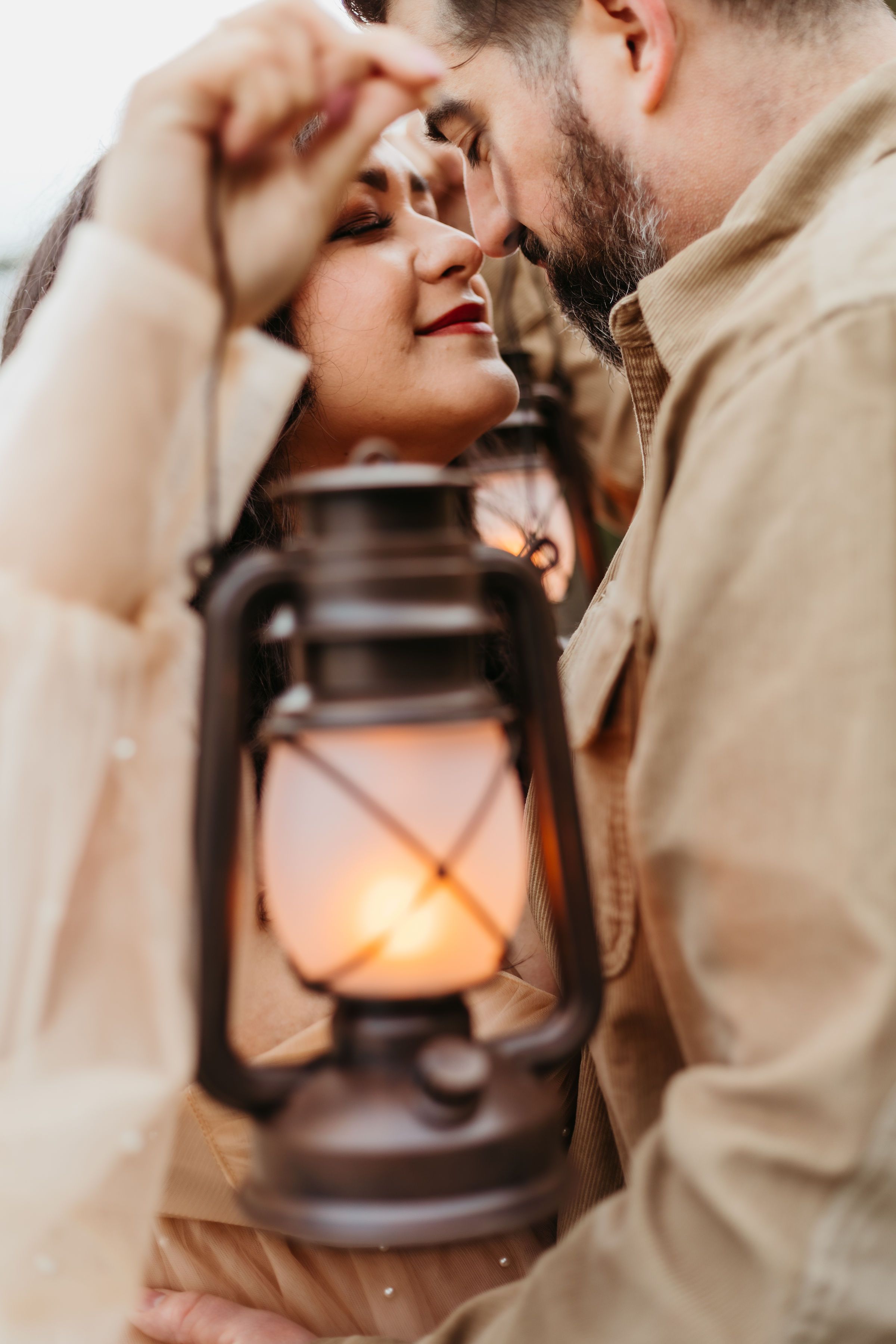 Romantic couple embraces near a glowing vintage lantern in soft focus lighting creating an intimate atmosphere.