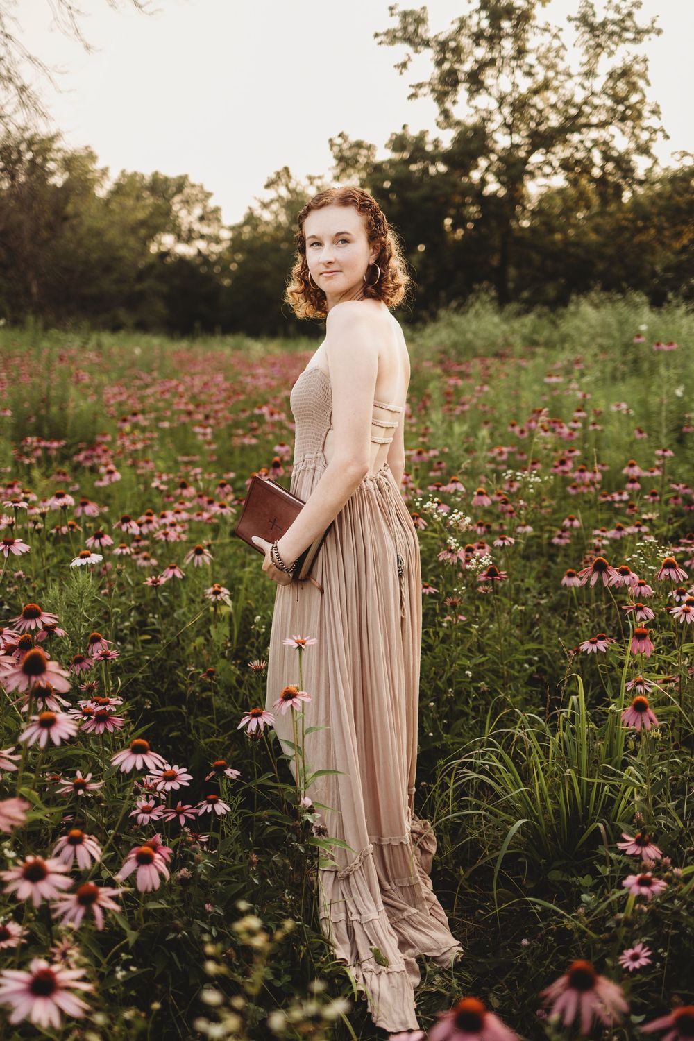 A woman in a flowing beige dress stands gracefully among blooming pink coneflowers at golden hour.
