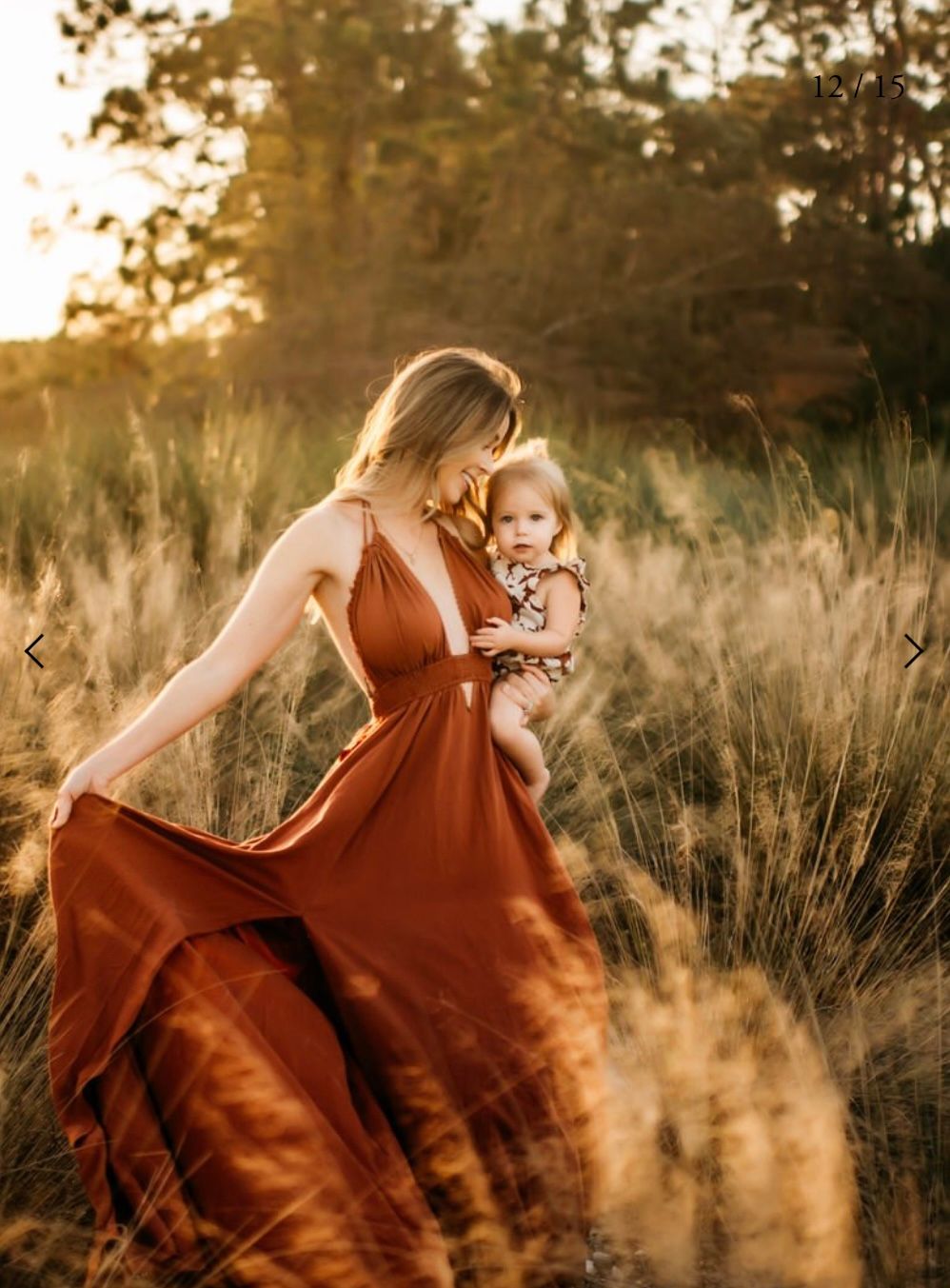 A woman in a flowing rust-colored dress twirls gracefully in a golden sunlit field of tall grass at sunset.