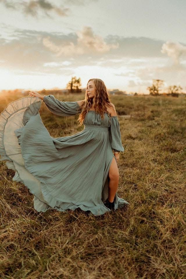 A flowing sage green dress billows dramatically in a golden sunset field during a romantic outdoor photoshoot.