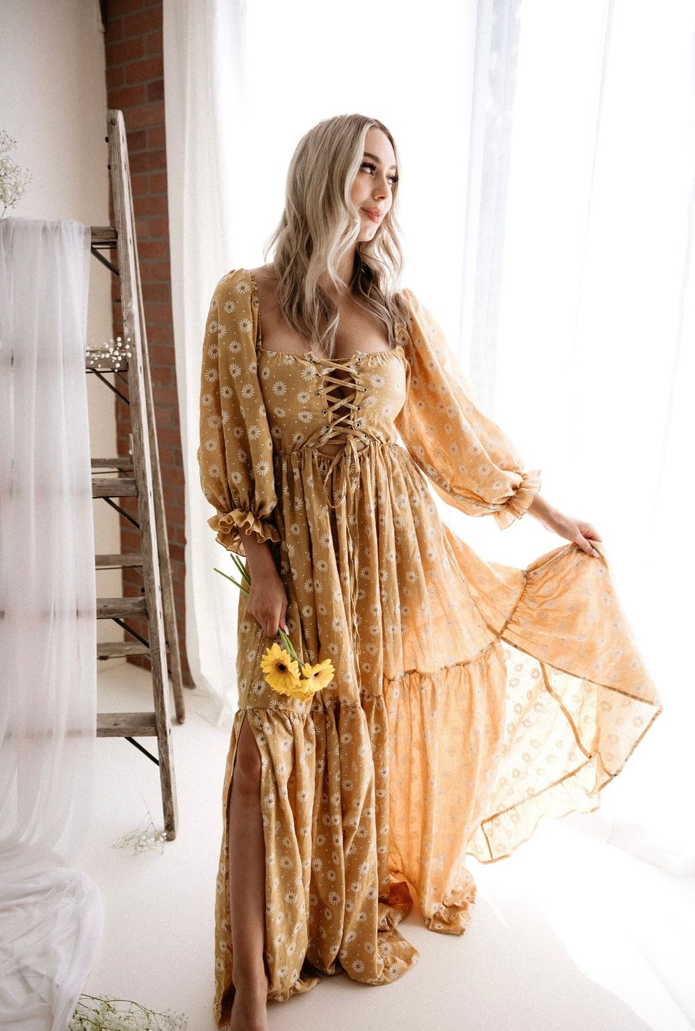 Ethereal boho photoshoot featuring a flowing golden velvet dress with bell sleeves against white curtains and natural light.