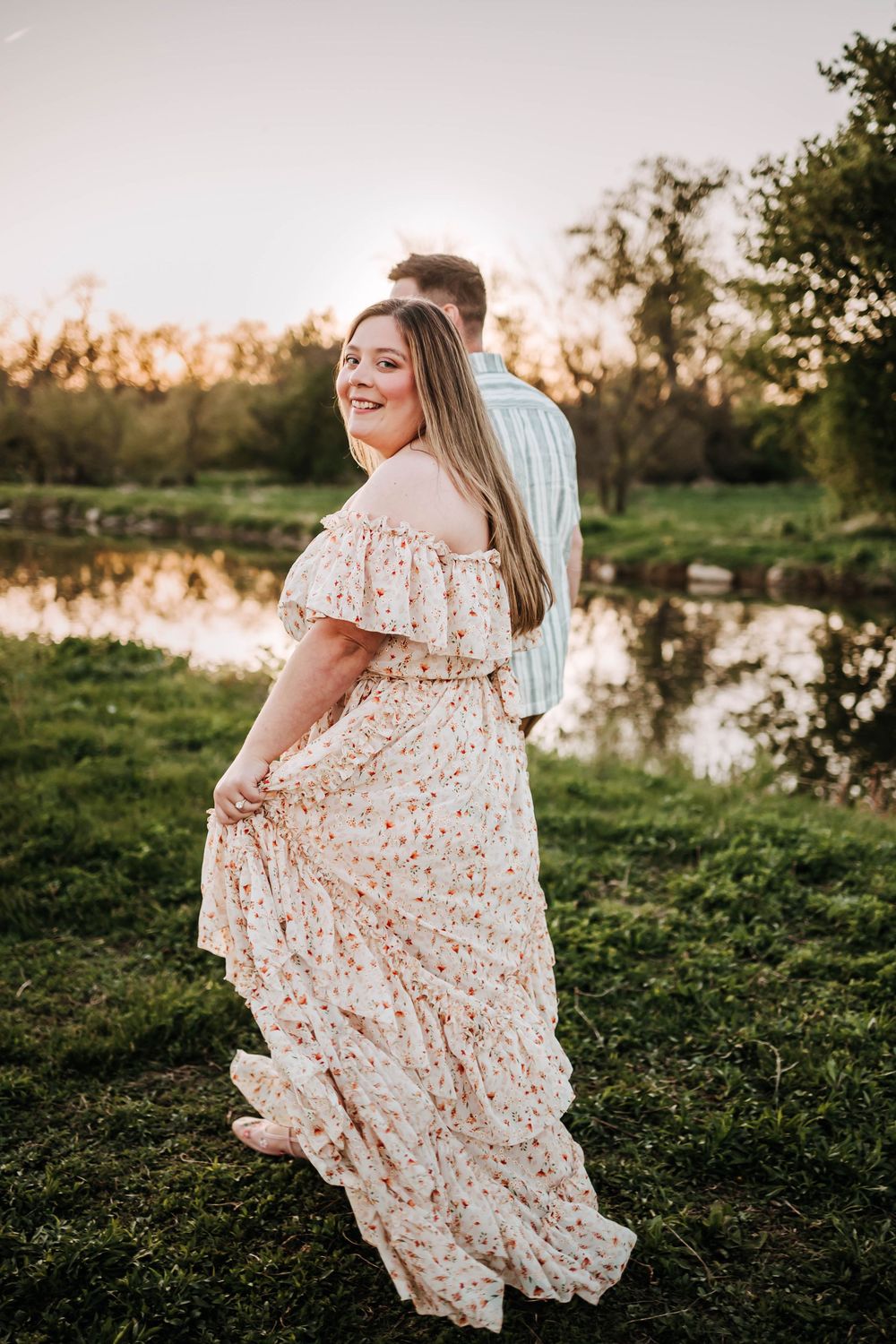A romantic sunset photoshoot by a pond featuring a flowing pink floral dress against a nature backdrop.
