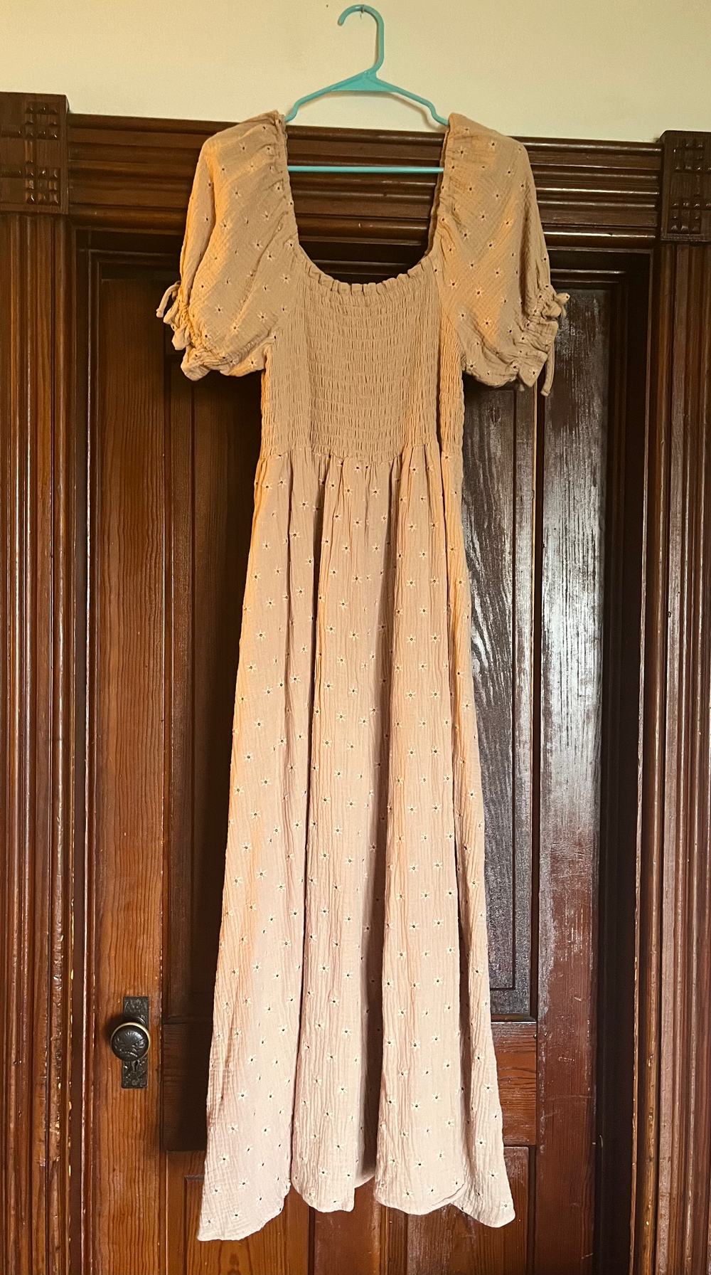 Tan smocked bodice midi dress with puff sleeves, small dot pattern, and flowing skirt hanging on a teal hanger.
