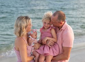 A happy family in shades of pink snuggle and giggle with the ocean behind them in Perdido Key