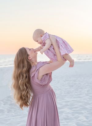 A mother holds her baby girl on the white sand beach at sunset in Pensacola.