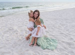A mother holds her daughters close while sitting on the white sand in Gulf Shores, Alabama