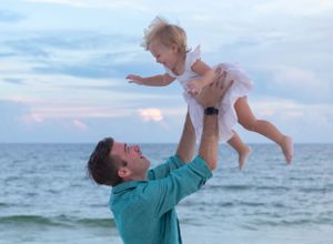 A dad tosses his little girl into the air with a sunset sky behind them in Gulf Shores