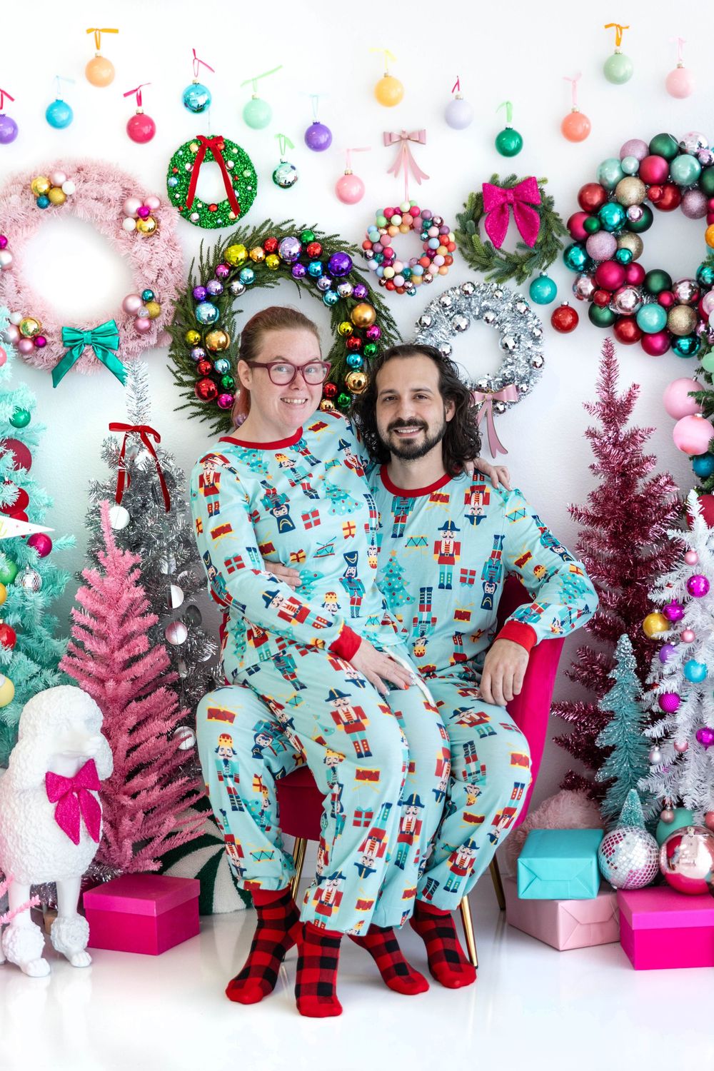 A couple poses in a pink Christmas studio setting.