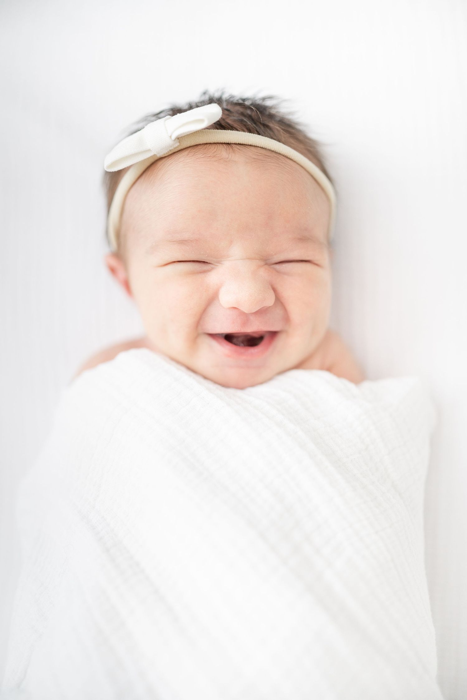 little boy with white swaddle wrapped around him, laying on white crib sheet naturally posed and sleeping
