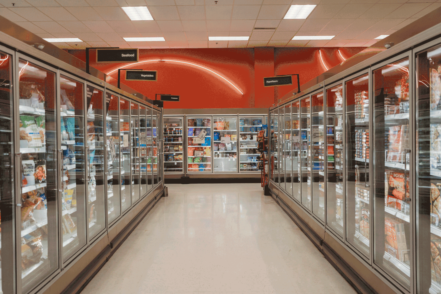 Long aisle of commercial freezer cases filled with frozen foods at a modern supermarket with bright lighting and orange trim.