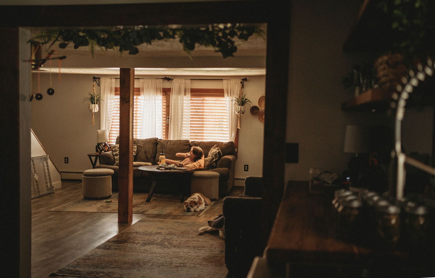 Warm sunlight streams into a cozy rustic living room with wooden beams and soft furnishings.