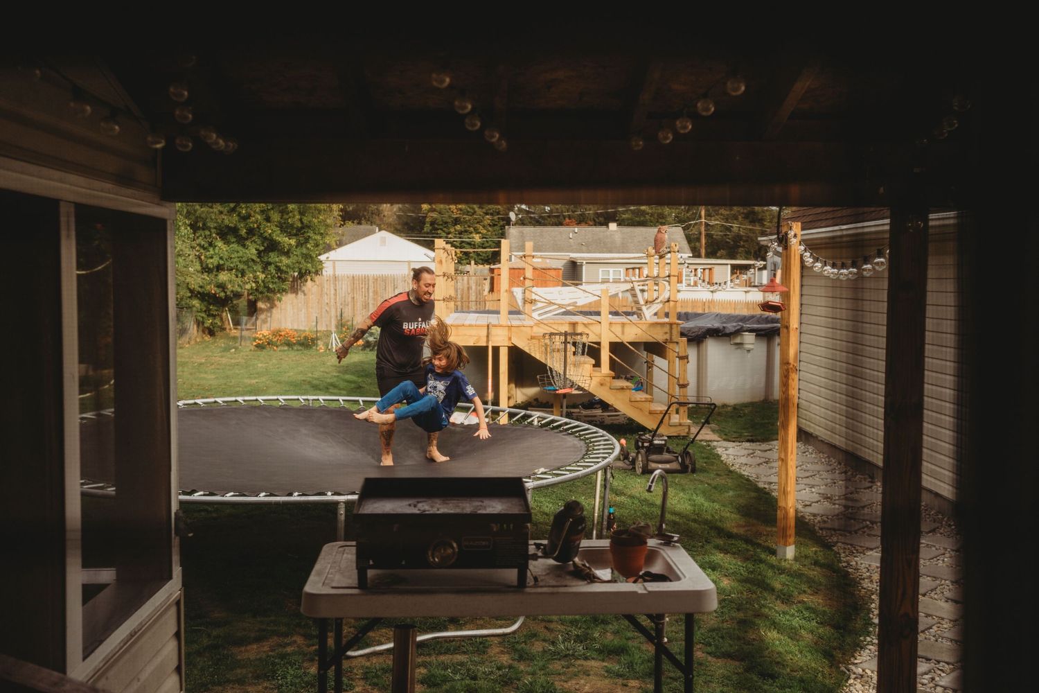 Workshop craftsman sanding and finishing wood on an outdoor covered patio with power tools and workbench.