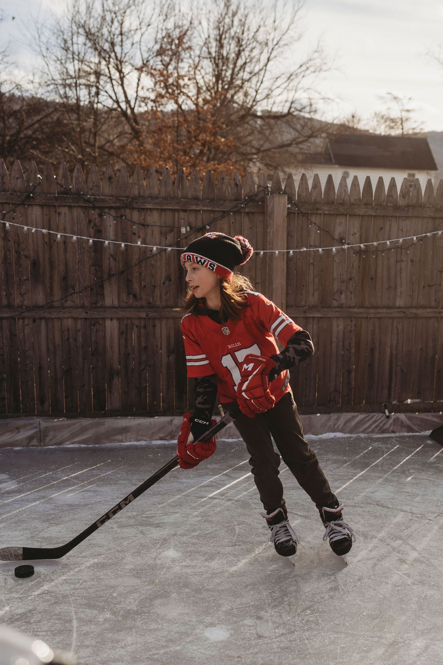 Hockey player practicing stick handling drills on a backyard ice rink with string lights hung overhead.