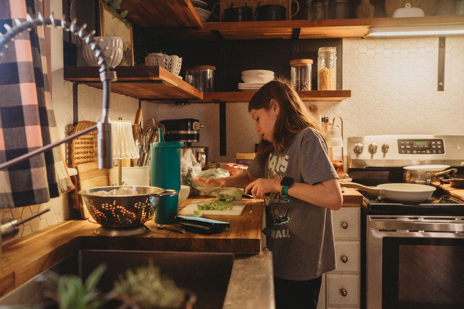 Person cooking in a warm, rustic kitchen with wooden countertops and modern appliances during evening hours.