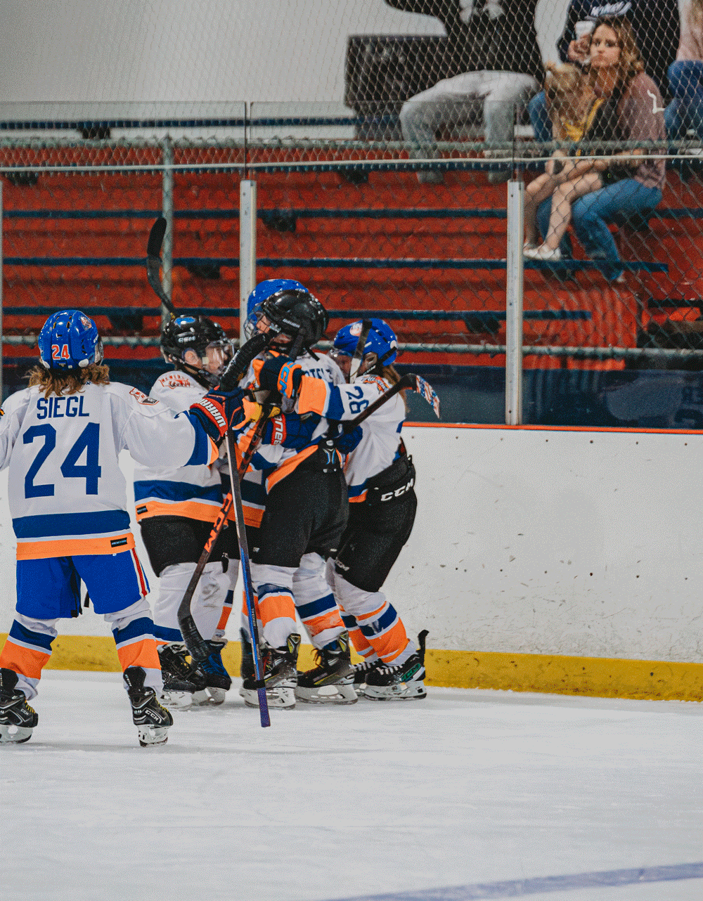 Hockey players from opposing teams in blue and orange uniforms battle for possession during an ice hockey match.