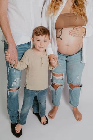 Family maternity photo with young child in beige shirt between parents wearing distressed denim.