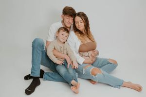 Family in casual denim sits together on studio floor during intimate portrait session.