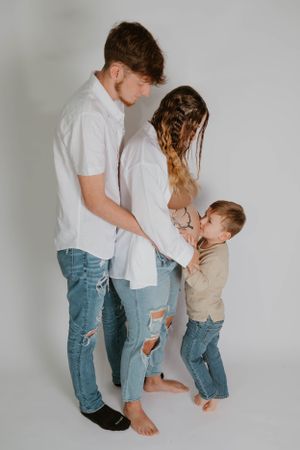 Family stands together in studio wearing coordinating white shirts and denim.