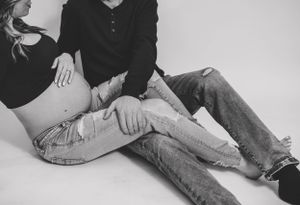 A black and white studio photo of a couple in casual wear sitting together.
