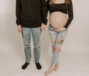 A couple holds hands during maternity photoshoot wearing matching casual outfits with distressed denim.