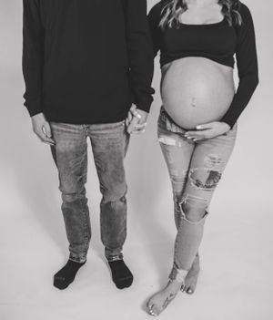 Black and white maternity portrait showing couple in casual wear against light background.