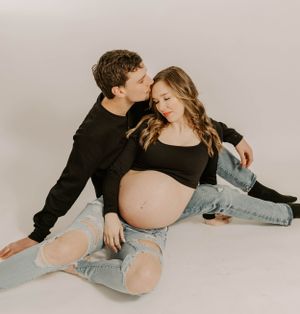 Intimate maternity portrait with couple in casual wear sharing tender moment on studio floor.