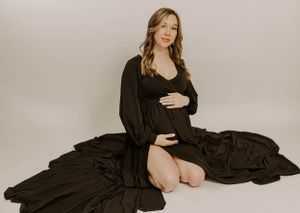Elegant maternity portrait with woman in black dress posed against neutral background.