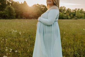 A silhouetted figure in a flowing dress stands in a sunlit meadow at golden hour.