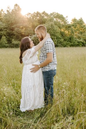 Romantic maternity photo of couple embracing in tall grass during sunset.