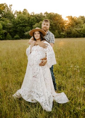 Intimate maternity portrait of couple in field with flowing white dress and golden light.