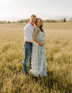 Expecting couple embracing in sunset-lit field wearing casual and formal attire.