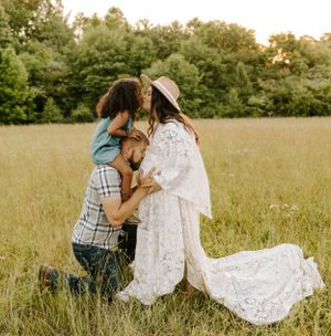 Family shares tender moment in sunlit field during maternity photoshoot.