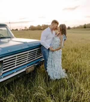 Couple in romantic pose by vintage blue truck in rustic field setting.
