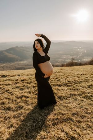 Silhouetted pregnant woman poses gracefully against mountain landscape at sunset.