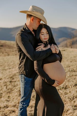 Intimate maternity moment captured on hillside during golden hour.