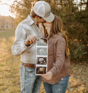 Couple sharing intimate moment while holding ultrasound photos in golden sunset light.