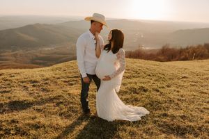 Couple shares tender moment on hilltop during sunset maternity photoshoot.