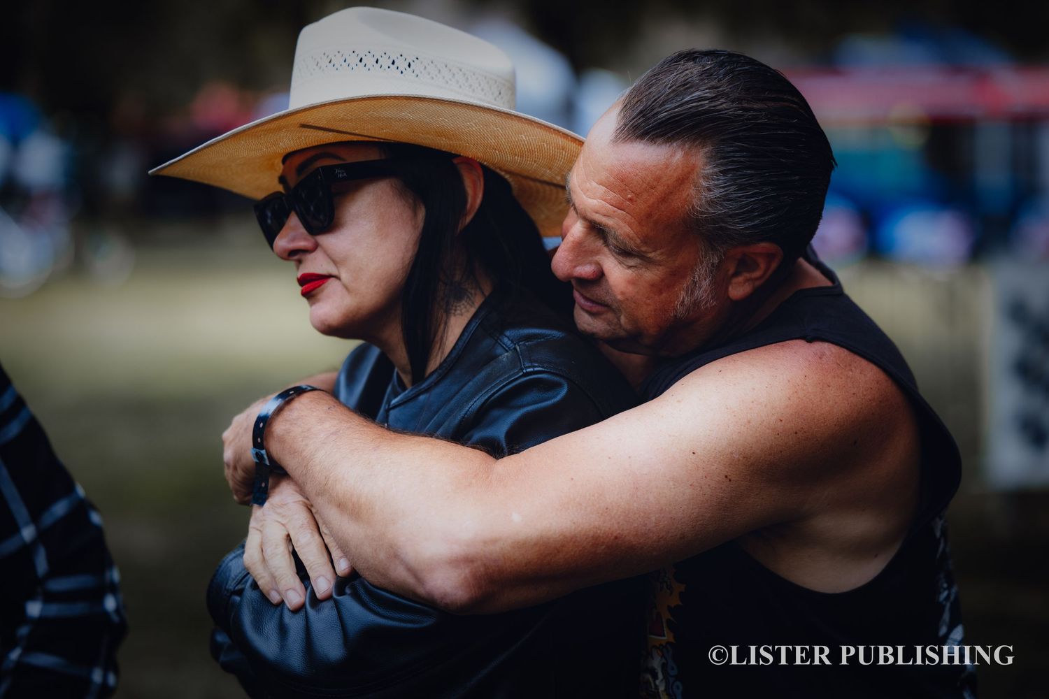 Two people share an intimate moment at an outdoor event wearing western attire.