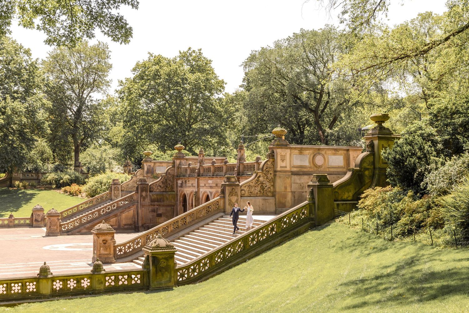 Couple in wedding attire poses on ornate stone staircase at Bethesda Terrace in Central Park, NYC.