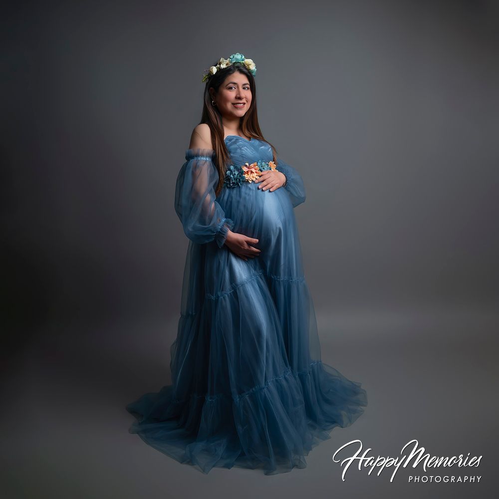 Pregnant woman in blue tulle maternity gown with floral crown poses gracefully in professional studio photography session.