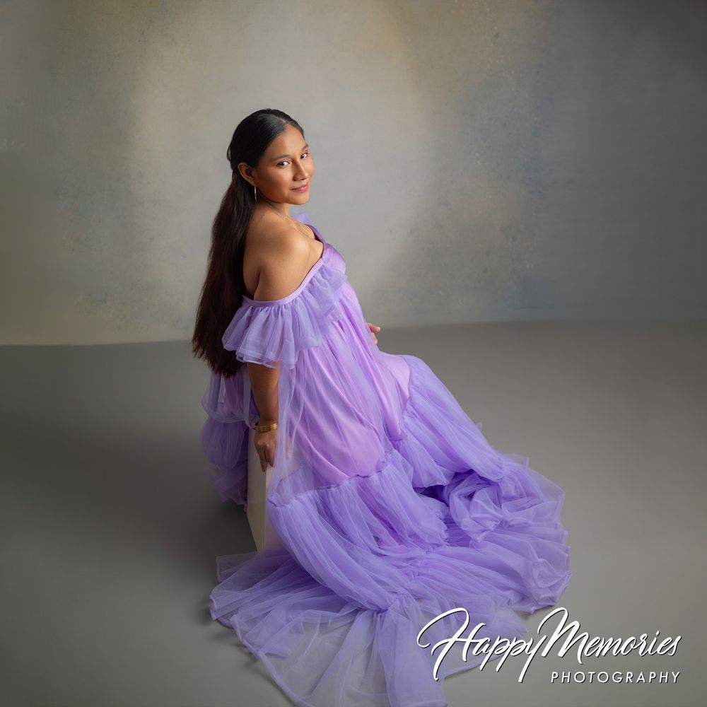 Pregnant woman in lavender tulle off-shoulder gown poses gracefully in a professional maternity photography studio session.