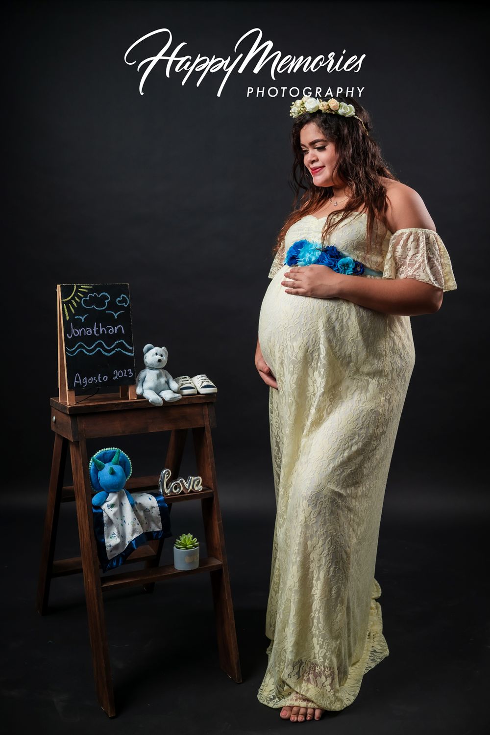 Studio maternity photography with yellow lace dress and blue baby announcement props.