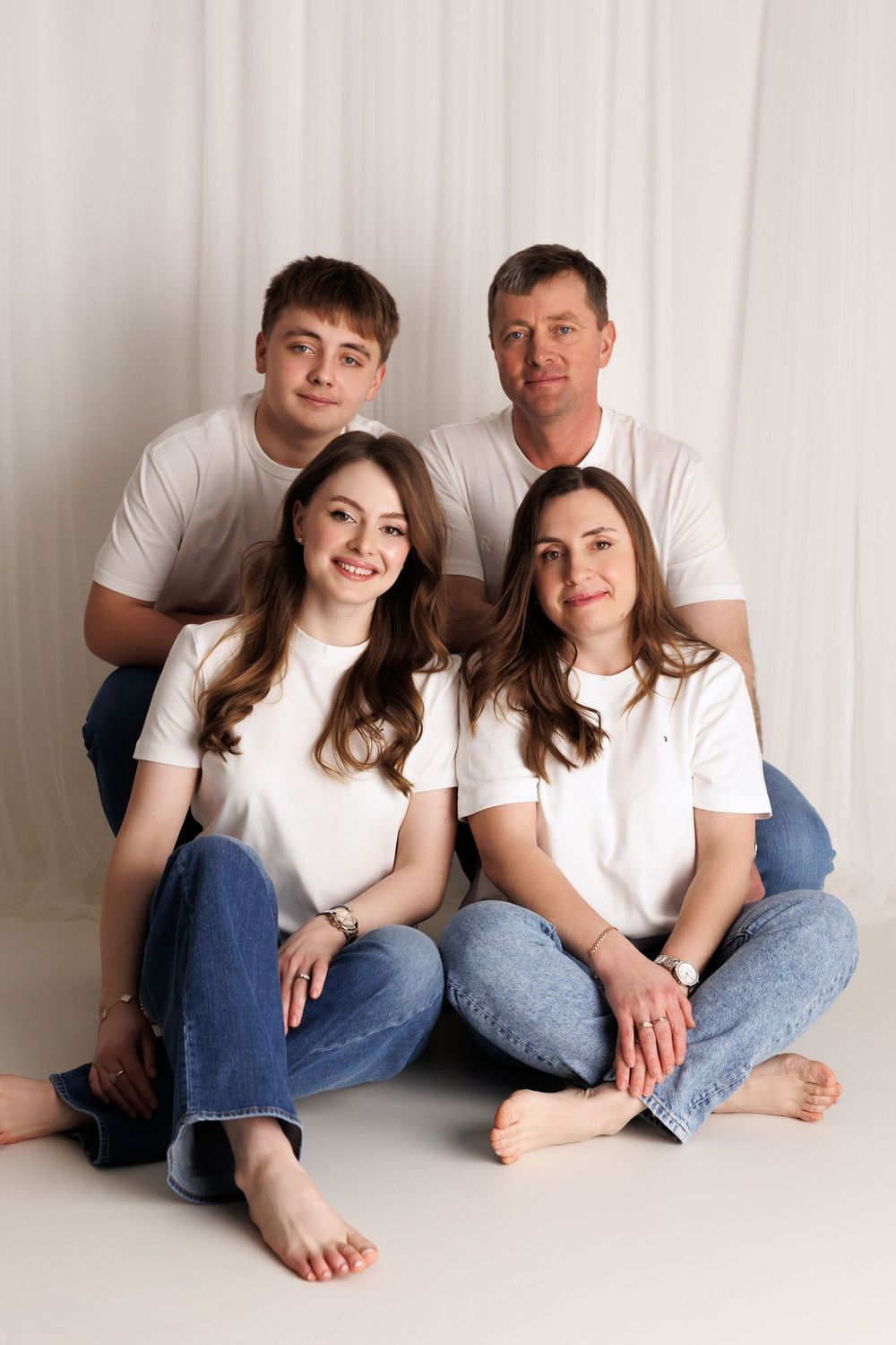 Family of four in matching white t-shirts and jeans posing together against a white backdrop.