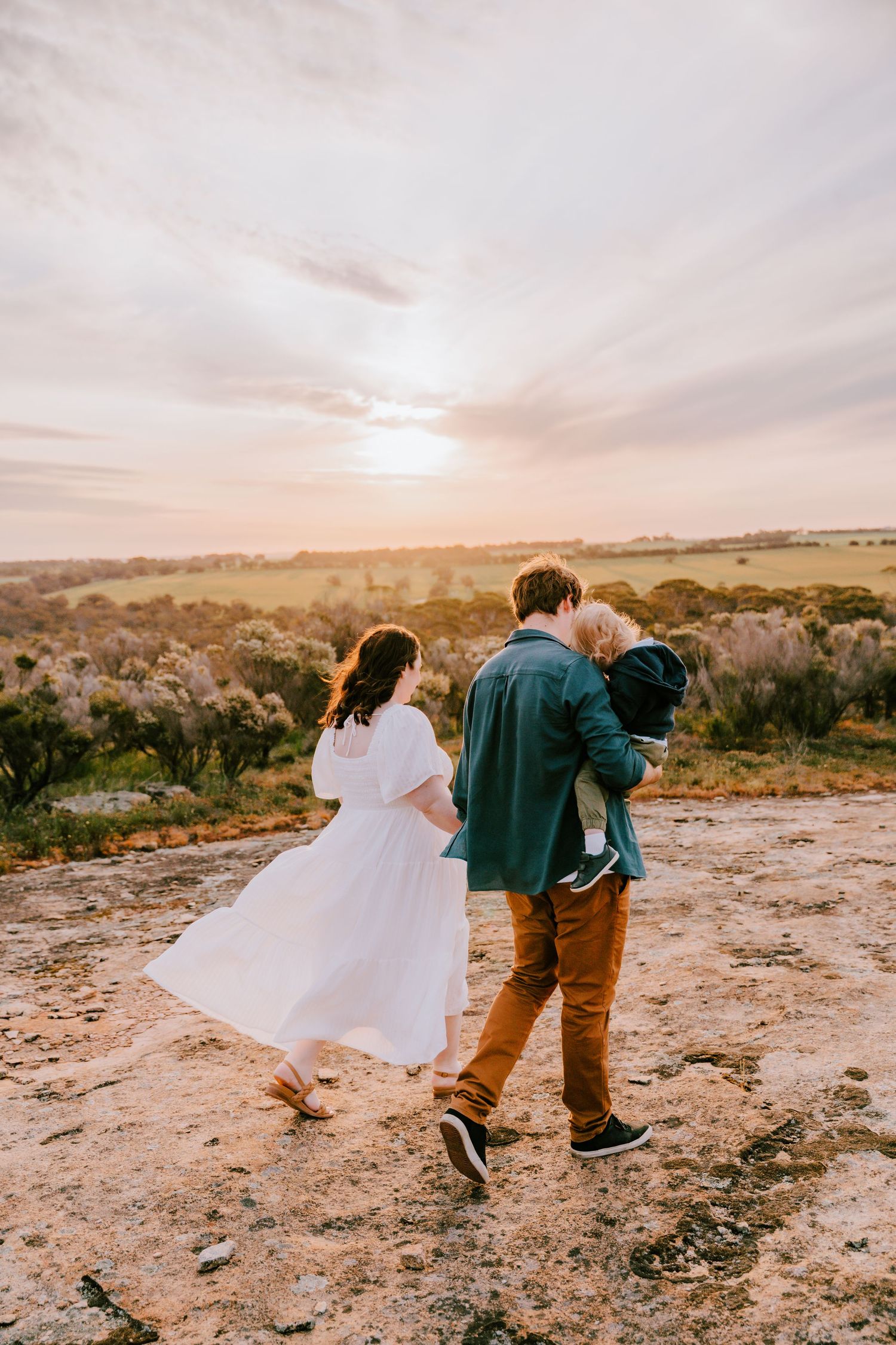 Wedding couple walking along a rocky cliff edge at sunset.