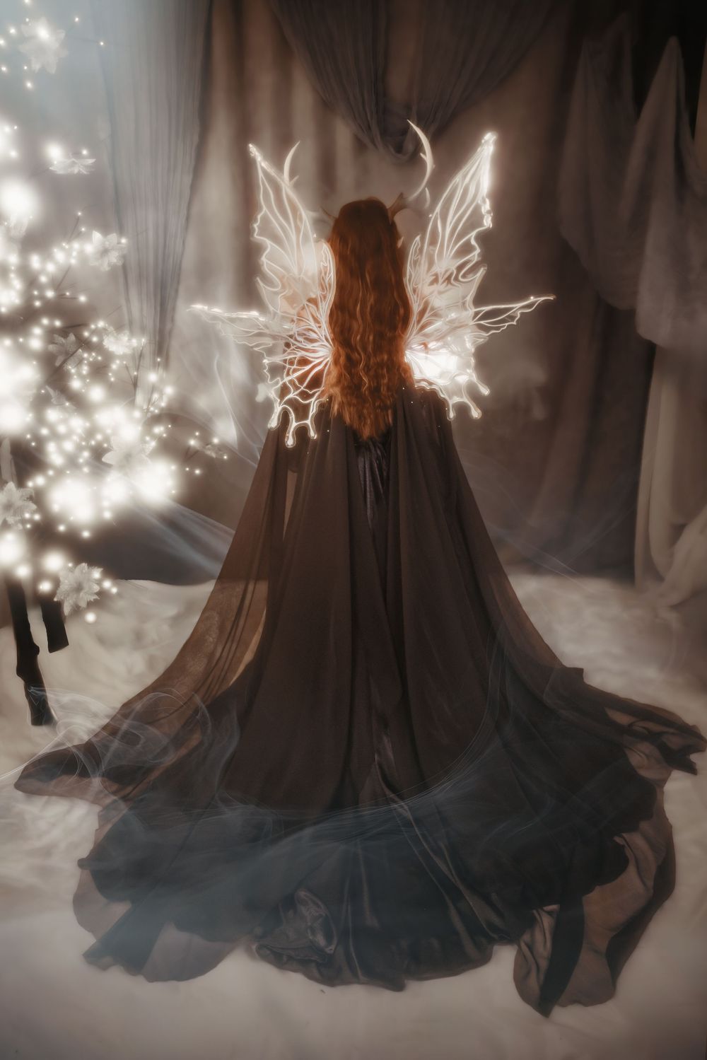 A figure in a flowing black dress with illuminated fairy wings stands in a dreamy, ethereal setting with twinkling lights.