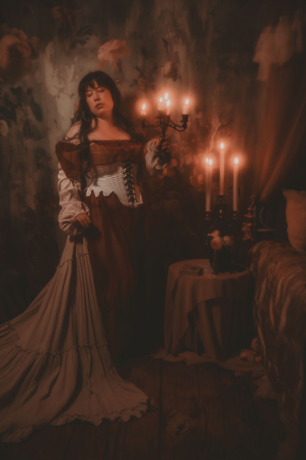 A woman in a Renaissance-era gown holds a candelabra with lit candles in a dark, moody, atmospheric setting.