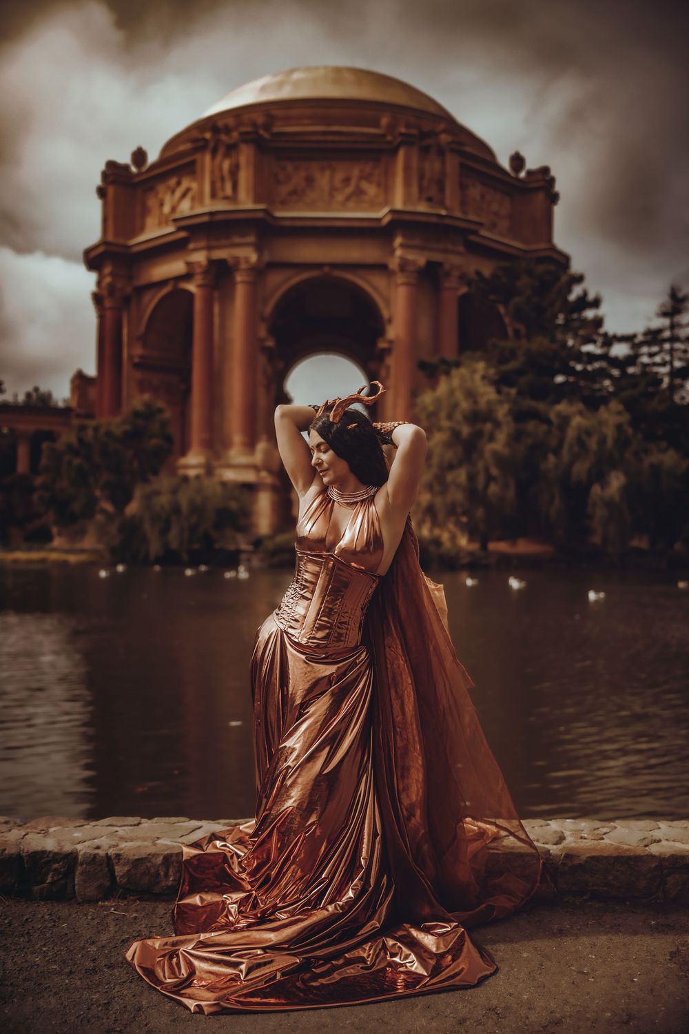 A figure in a flowing copper-colored dress poses dramatically by a reflecting pool at the Palace of Fine Arts in San Francisco.